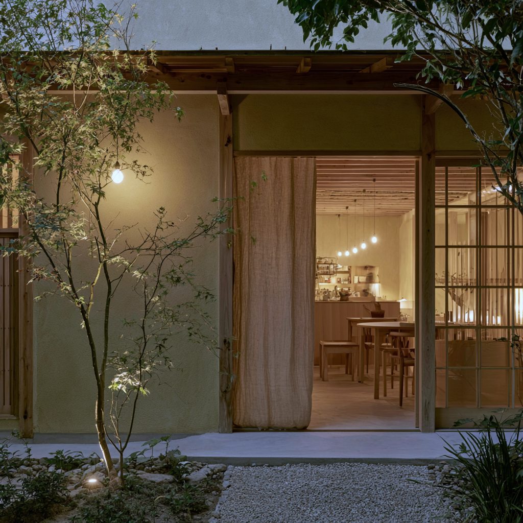 Plaster facade at dusk with a linen curtain at the open door and the lit dining room inside