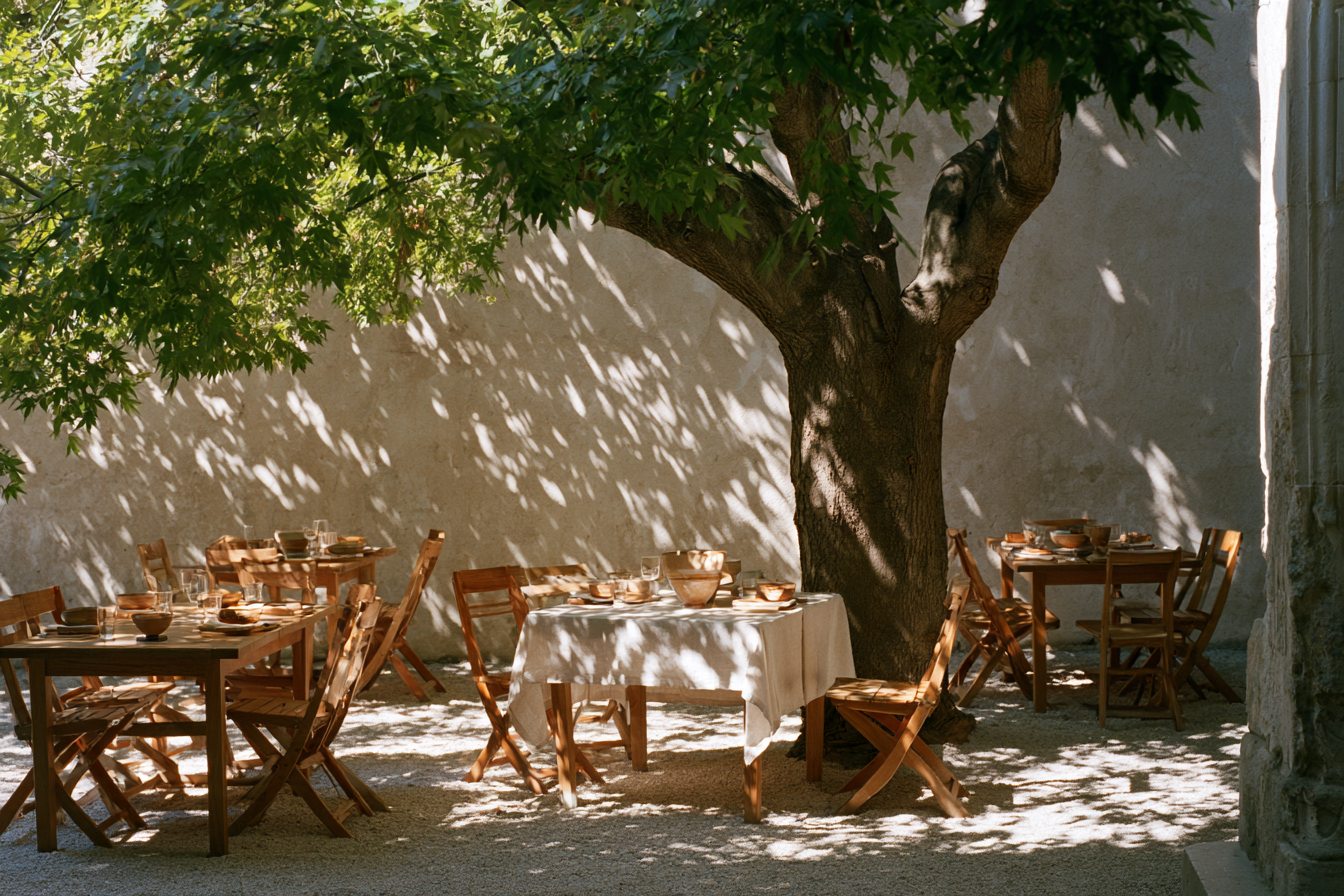 Courtyard terrace under a large tree, a table laid with white linen for a long lunch